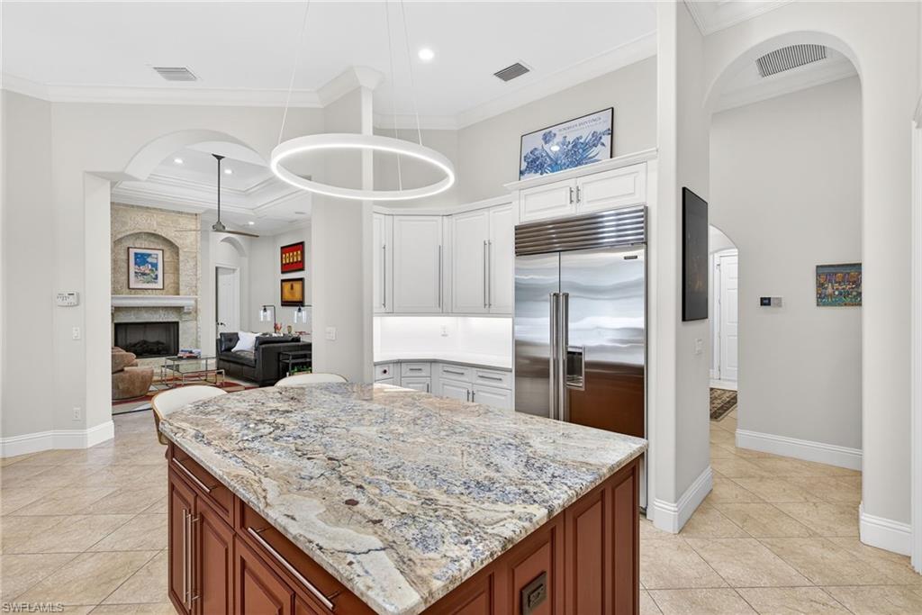 Kitchen featuring arched walkways, pendant lighting, light stone countertops, built in refrigerator, and open floor plan