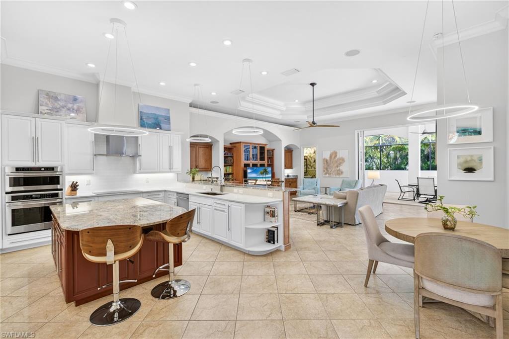 Kitchen with light stone counters, hanging light fixtures, a peninsula, two tone color scheme, and ornamental molding