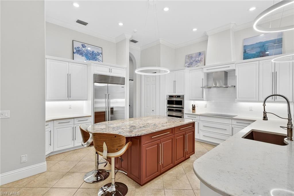 Dual tone kitchen with ornamental molding, light stone countertops, decorative backsplash, a center island, and stainless steel appliances
