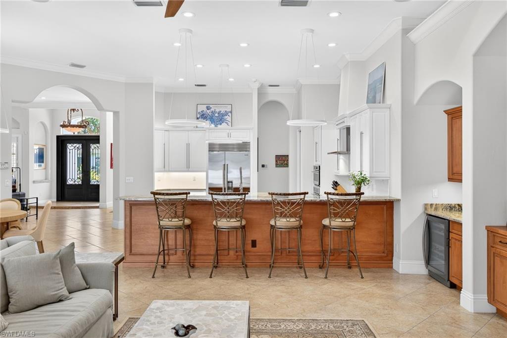 Kitchen with arched walkways, a kitchen bar, ornamental molding, a peninsula, and light stone countertops