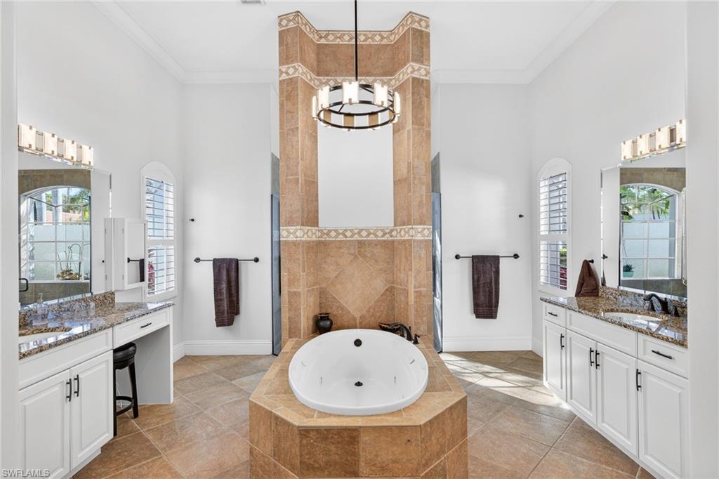 Bathroom featuring a high ceiling, two vanities, a whirlpool tub, walk in shower, and ornamental molding