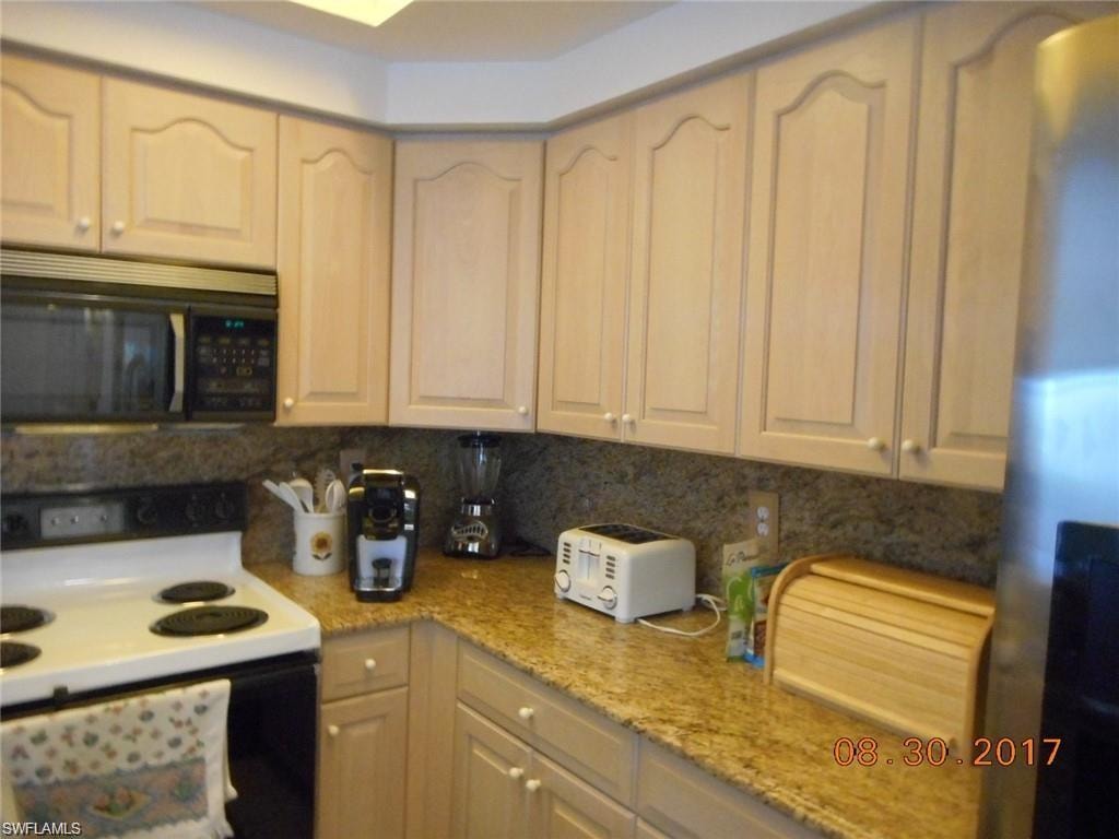 Kitchen with range with electric cooktop, stainless steel fridge with ice dispenser, light stone counters, and tasteful backsplash