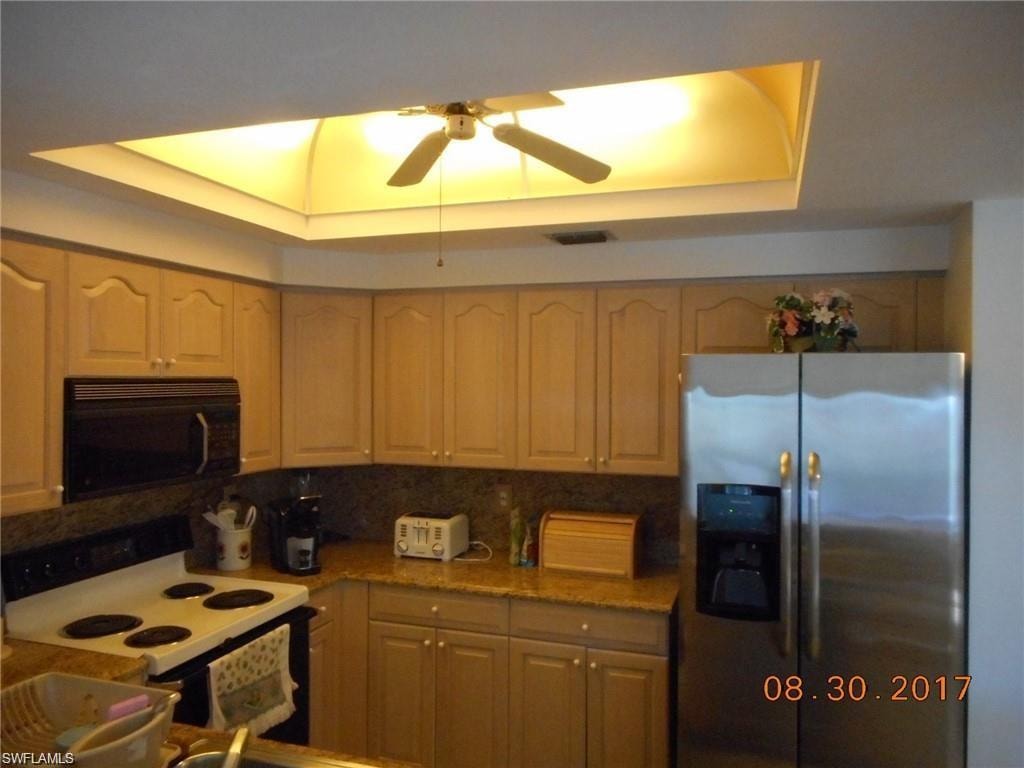 Kitchen featuring a tray ceiling, stainless steel fridge with ice dispenser, range with electric cooktop, black microwave, and ceiling fan
