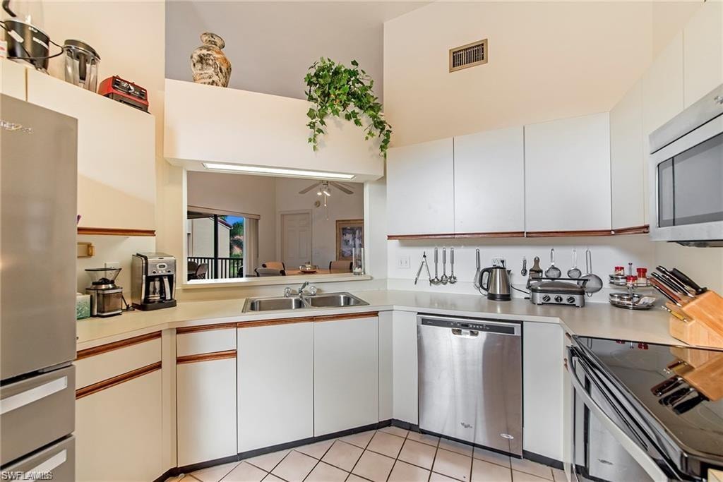 Dual tone kitchen with stainless steel appliances, light countertops, light tile patterned flooring, dual tone cabinets, and a ceiling fan