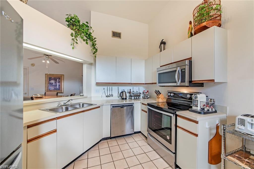 Kitchen with stainless steel appliances, light countertops, a ceiling fan, two tone cabinets, and light tile patterned floors