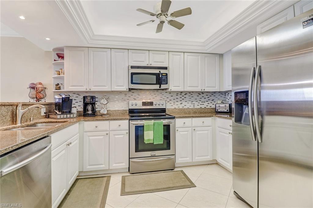 Kitchen featuring stainless steel appliances, light stone counters, white cabinetry, ornamental molding, and a ceiling fan
