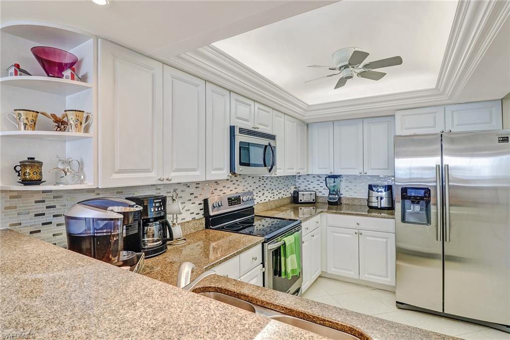 Kitchen featuring stainless steel appliances, open shelves, light stone counters, white cabinets, and ornamental molding