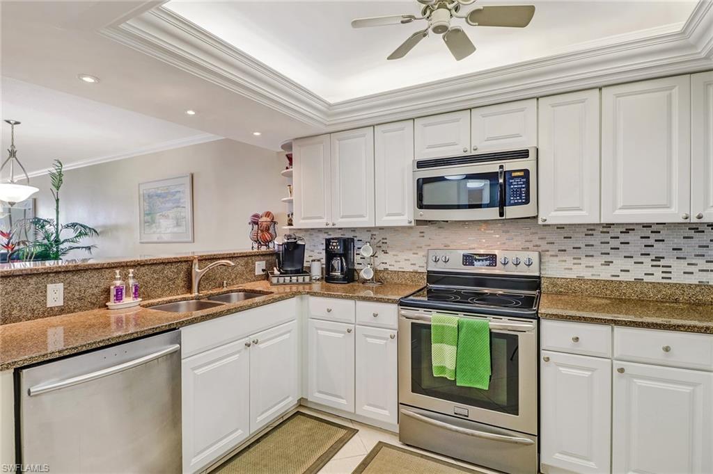 Kitchen featuring stainless steel appliances, ornamental molding, dark stone countertops, white cabinetry, and a raised ceiling