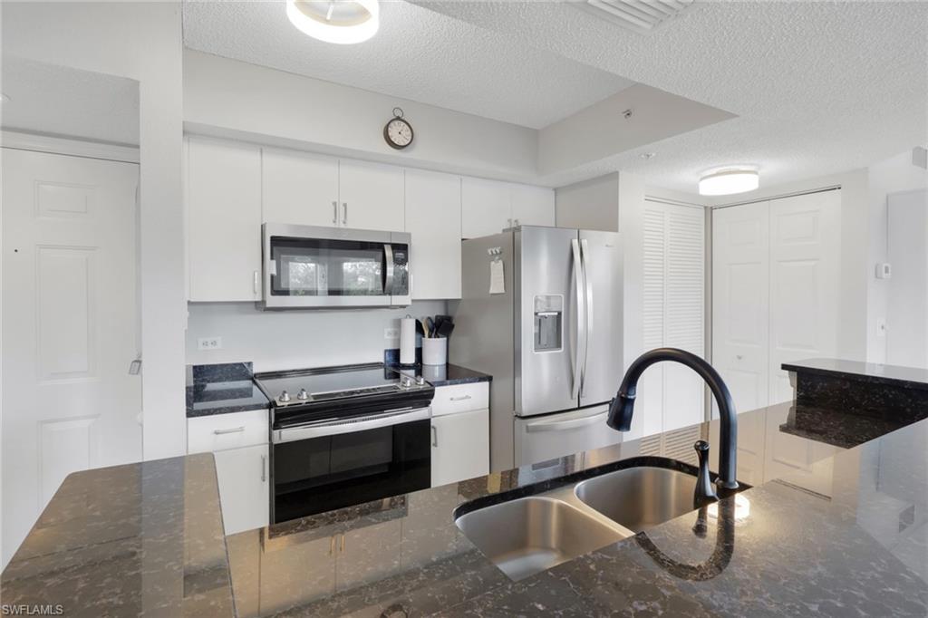 Kitchen with dark stone counters, stainless steel appliances, a textured ceiling, and white cabinetry