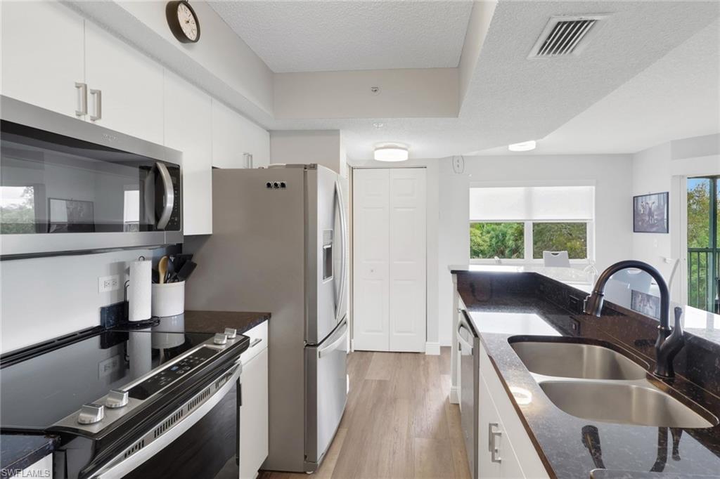 Kitchen with stainless steel appliances, white cabinets, dark stone counters, a textured ceiling, and light wood-style flooring