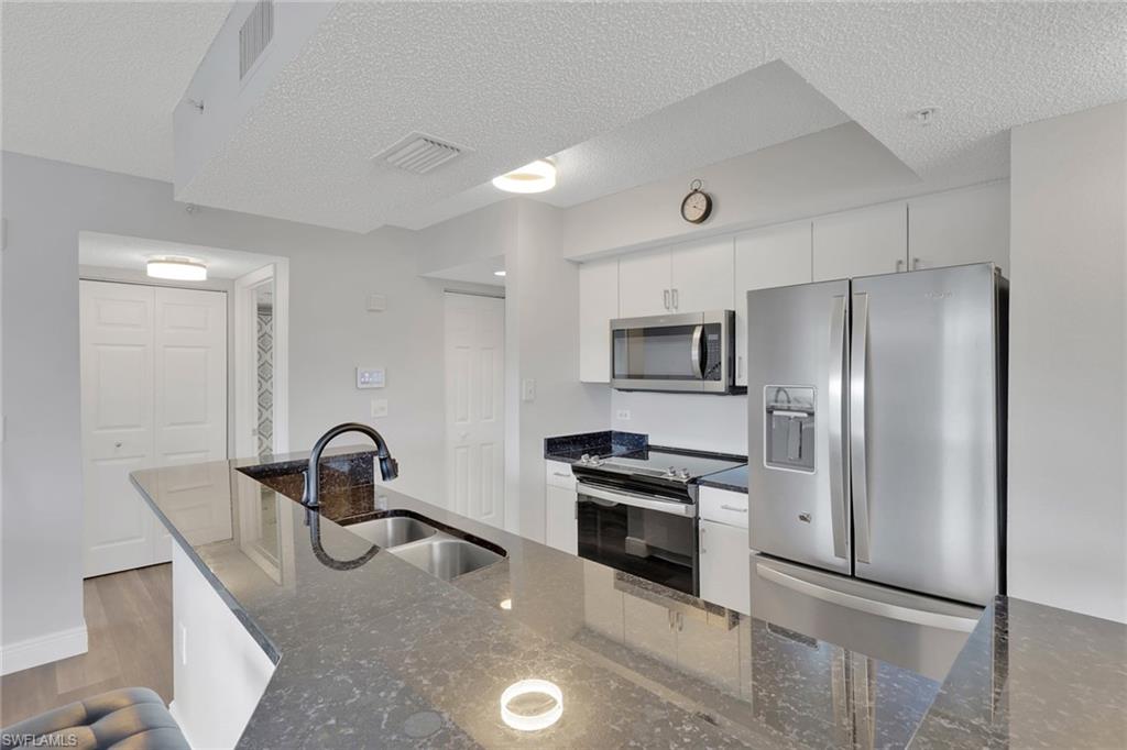 Kitchen with stainless steel appliances, dark stone countertops, white cabinetry, a textured ceiling, and light wood-style flooring