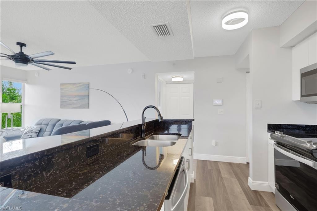Kitchen featuring dark stone counters, stainless steel appliances, dark wood-style flooring, white cabinetry, and a textured ceiling