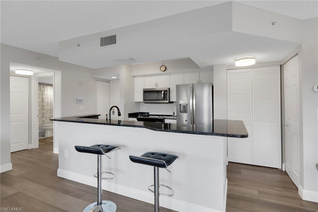 Kitchen with stainless steel appliances, a textured ceiling, dark wood-style floors, a breakfast bar, and white cabinets