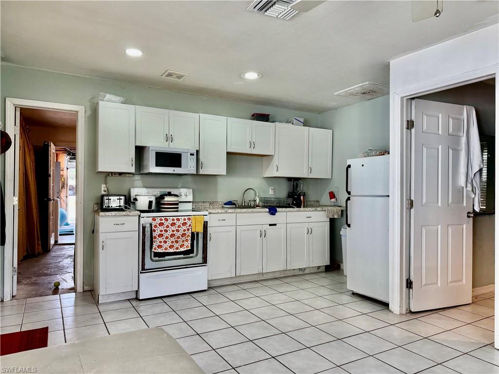 Kitchen with white cabinetry, white appliances, light countertops, and light tile patterned flooring