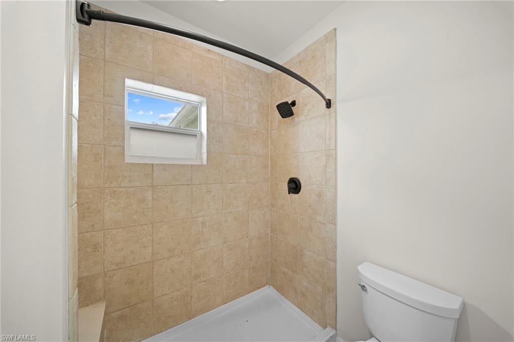 Tiled shower enclosure featuring a curved dark-finish shower rod, a dark-finish showerhead, and a fixed window