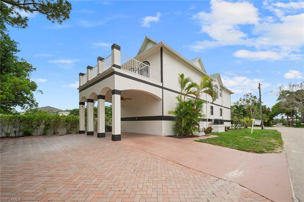 Exterior with elevated balcony, columned porte-cochère, paver driveway, stucco finish, and mature landscaping
