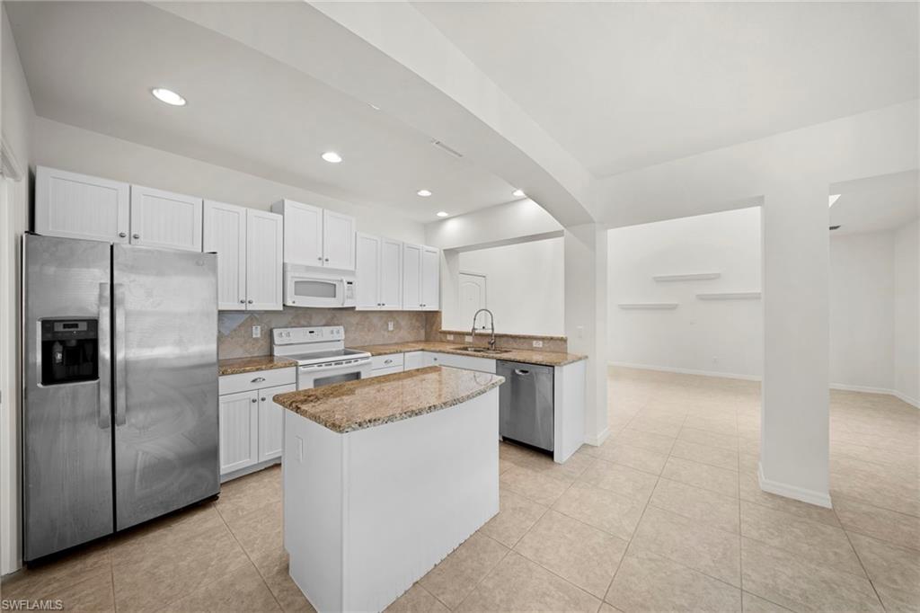 Kitchen featuring white cabinetry, stainless steel appliances, granite countertops, an island with a breakfast bar, and tile flooring