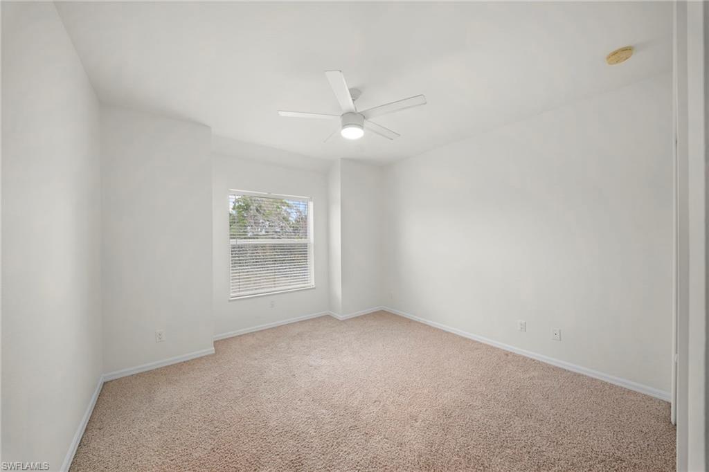 Neutral toned wall-to-wall carpeting in a bright room featuring a ceiling fan with integrated lighting