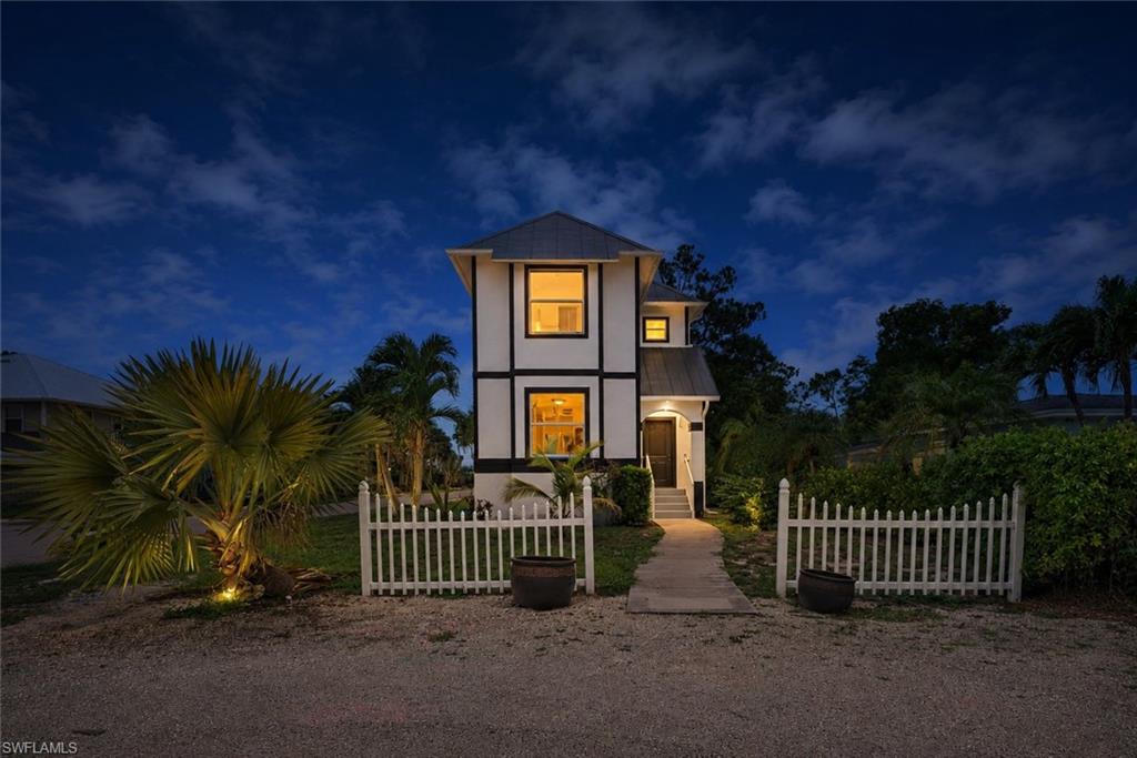 Two-story residence featuring white siding with dark trim, a metal roof, and lighted windows