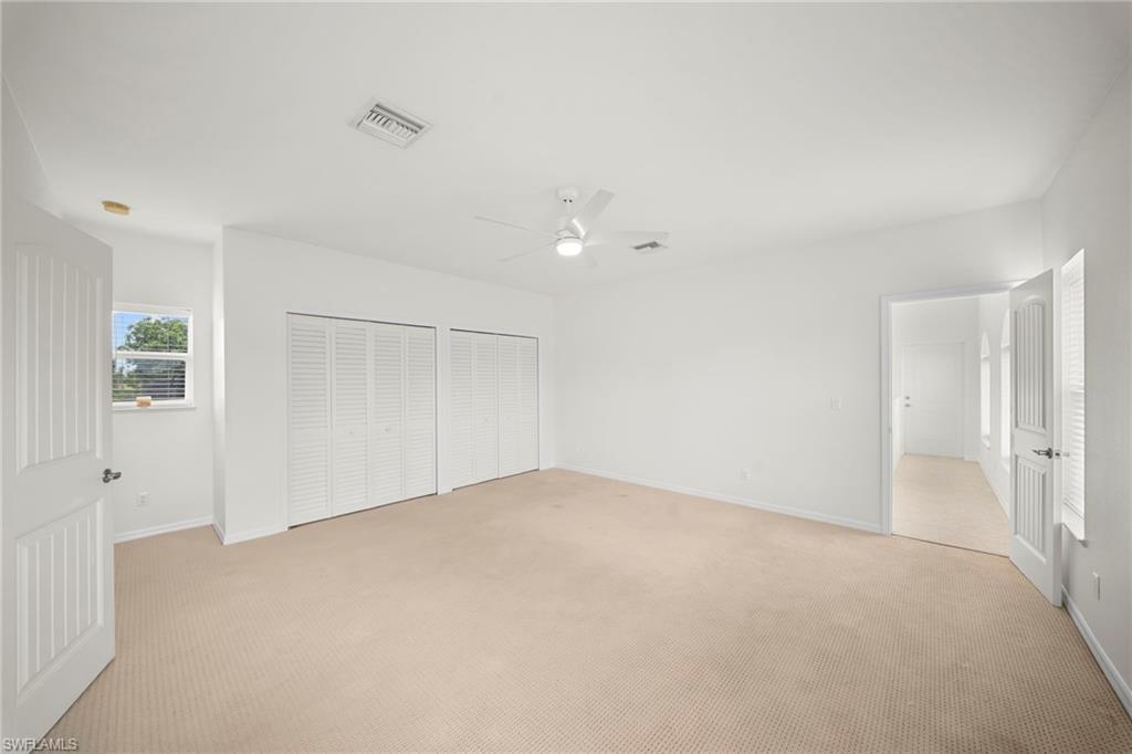 Spacious room featuring neutral carpeting, white walls, two louvered bifold closet doors, a ceiling fan, and a window with horizontal blinds
