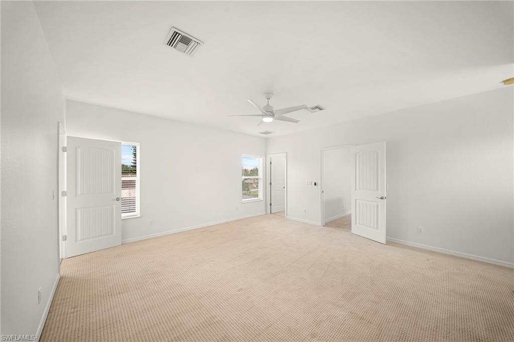 Spacious room with light-toned carpet flooring, a ceiling fan, and multiple windows providing natural illumination