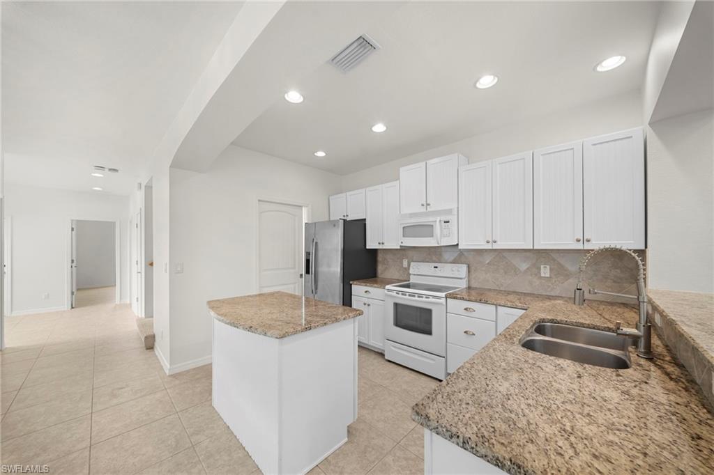 Bright kitchen featuring white cabinetry, granite countertops, stainless steel appliances, a center island, and tile flooring