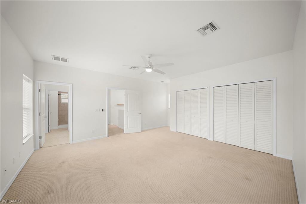 Spacious room featuring neutral carpeting, a ceiling fan, multiple louvered closet doors, and white walls