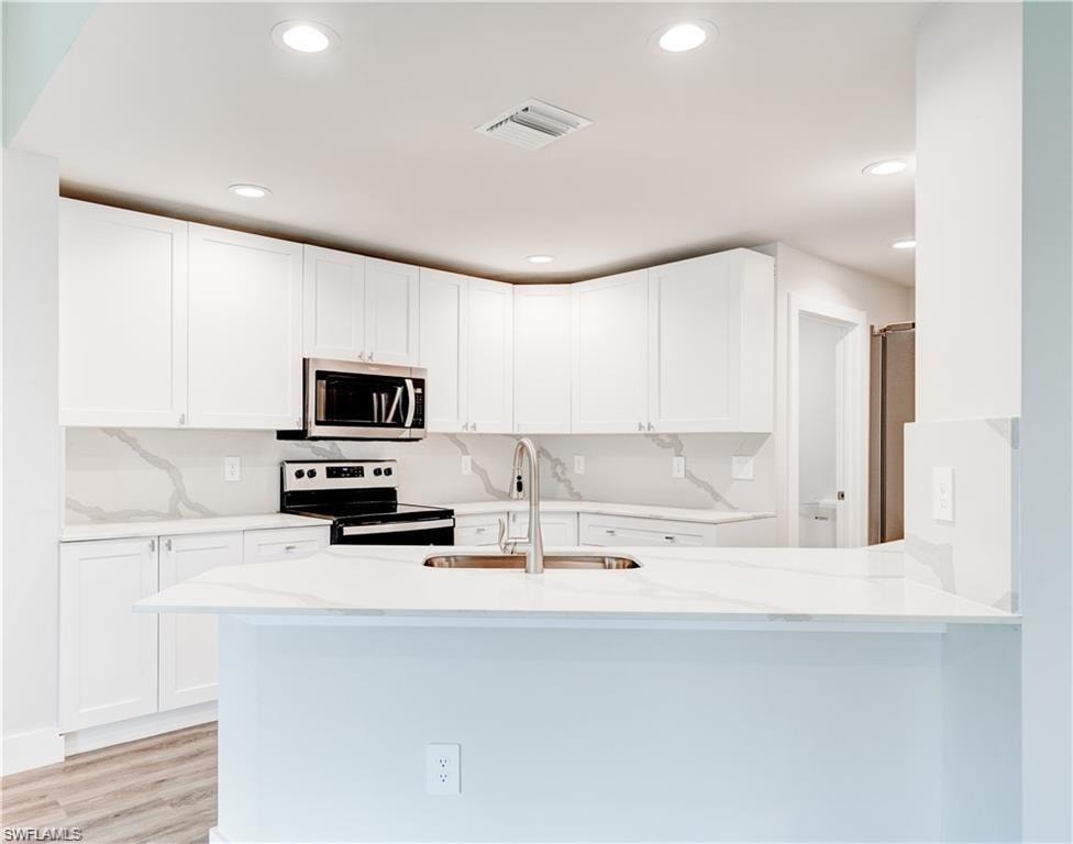 Kitchen featuring stainless steel appliances, white cabinets, light stone counters, a peninsula, and recessed lighting