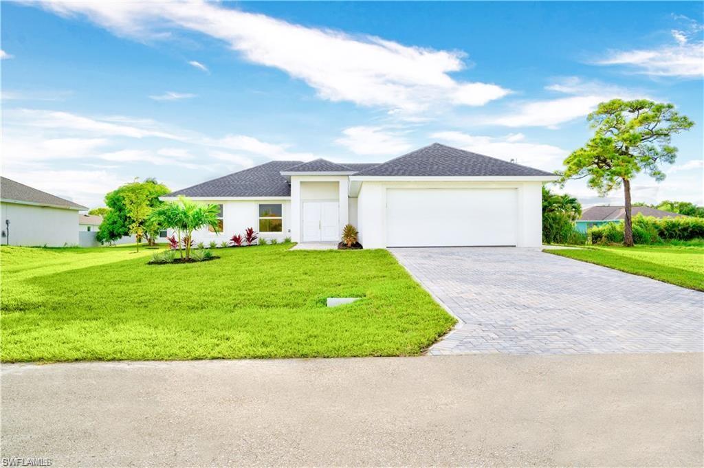 View of front of home with a front lawn, driveway, an attached garage, roof with shingles, and stucco siding