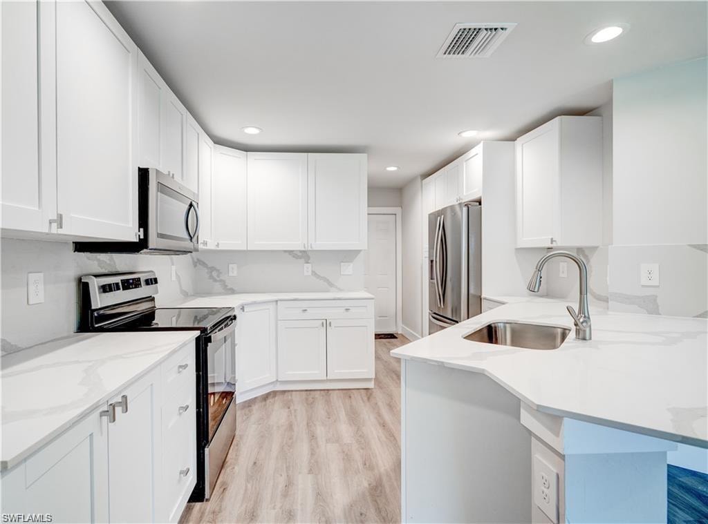 Kitchen featuring stainless steel appliances, light wood-style flooring, white cabinetry, light stone countertops, and recessed lighting