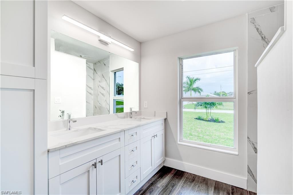 Full bath with double vanity, dark wood-style flooring, and a marble finish shower