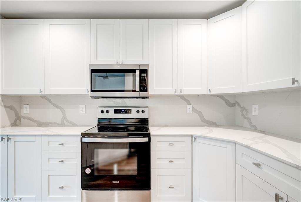 Kitchen with stainless steel appliances, white cabinetry, and light stone counters