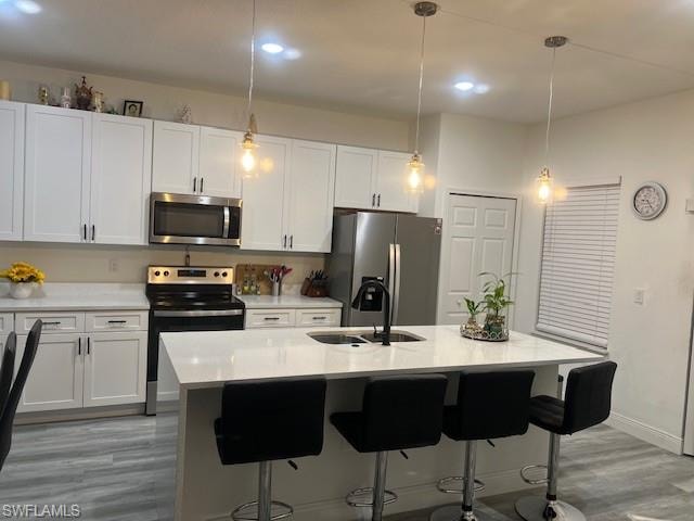 Kitchen featuring stainless steel appliances, a kitchen bar, light stone counters, white cabinetry, and hanging light fixtures