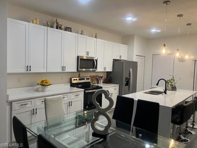 Kitchen featuring a breakfast bar, hanging light fixtures, stainless steel appliances, white cabinets, and light stone counters