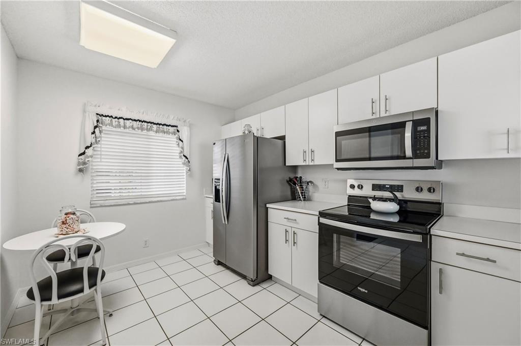 Kitchen featuring stainless steel appliances, light countertops, white cabinetry, light tile patterned flooring, and a textured ceiling