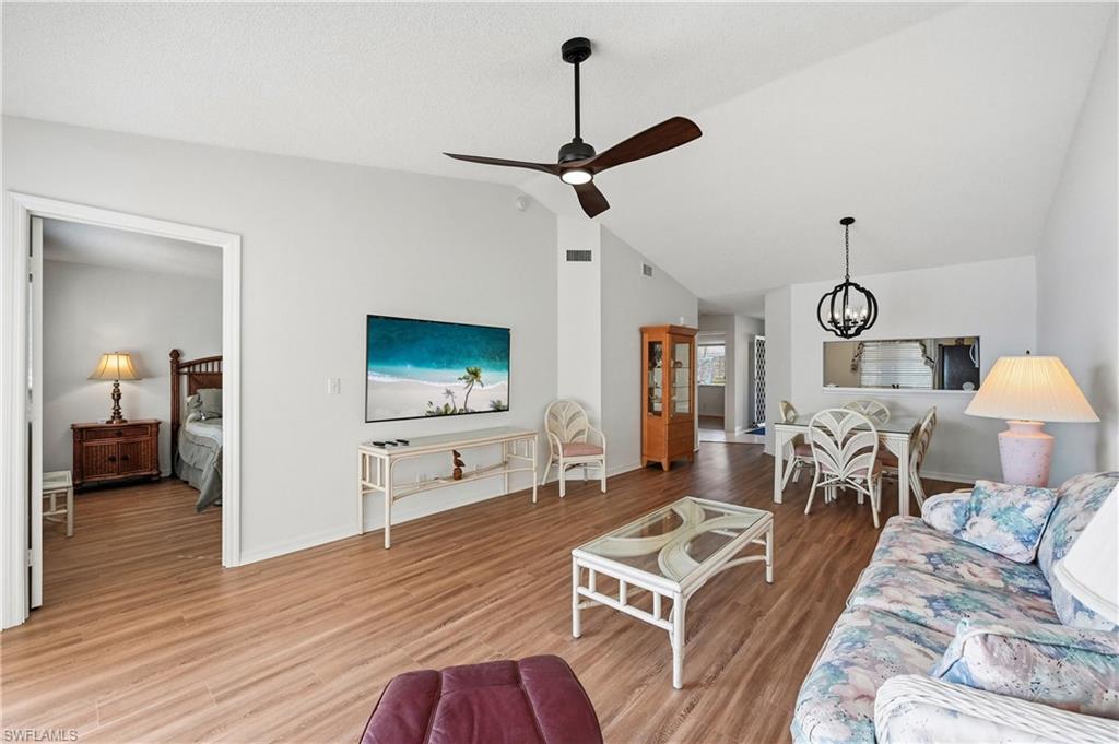 Living room with a chandelier, wood finished floors, lofted ceiling, and ceiling fan
