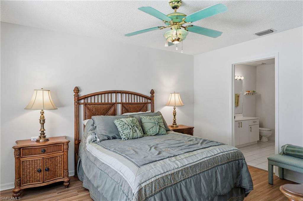 Bedroom with ceiling fan, ensuite bath, light wood-style floors, and a textured ceiling