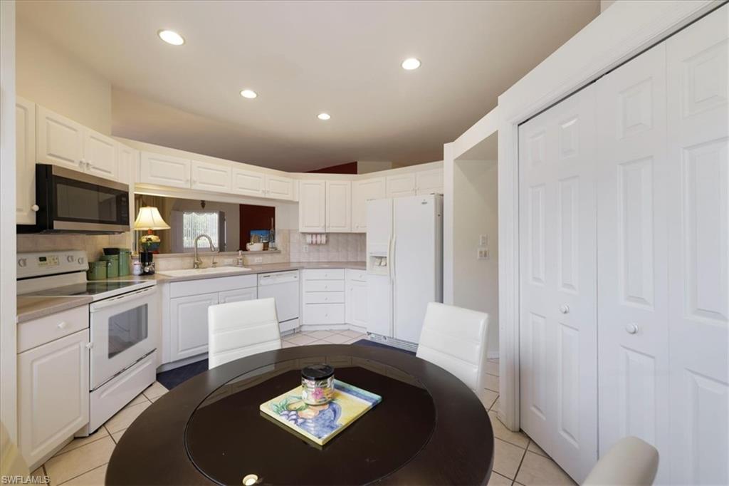 Kitchen with white appliances, tasteful backsplash, light countertops, white cabinets, and recessed lighting