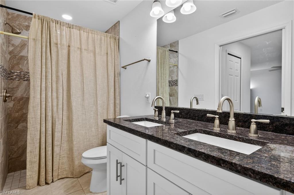 Primary bathroom with a tile shower, double vanity, and light tile patterned floors