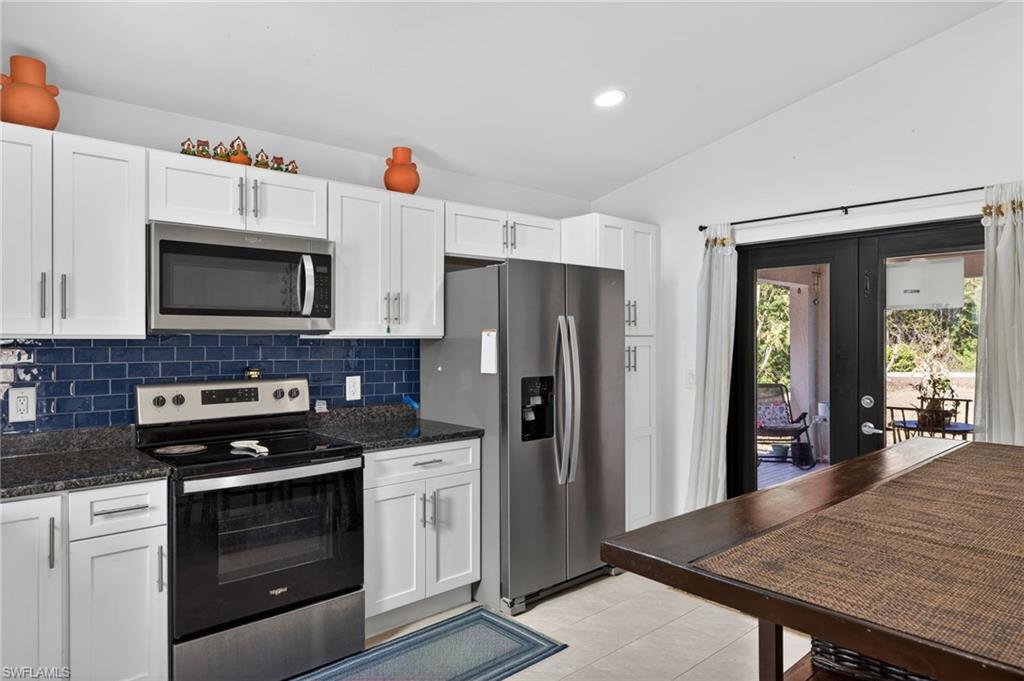 Kitchen with stainless steel appliances, white cabinets, vaulted ceiling, dark stone countertops, and tasteful backsplash