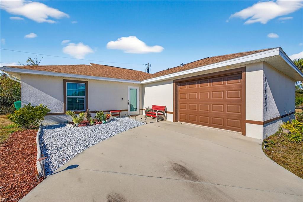 Ranch-style house featuring driveway, stucco siding, an attached garage, and roof with shingles