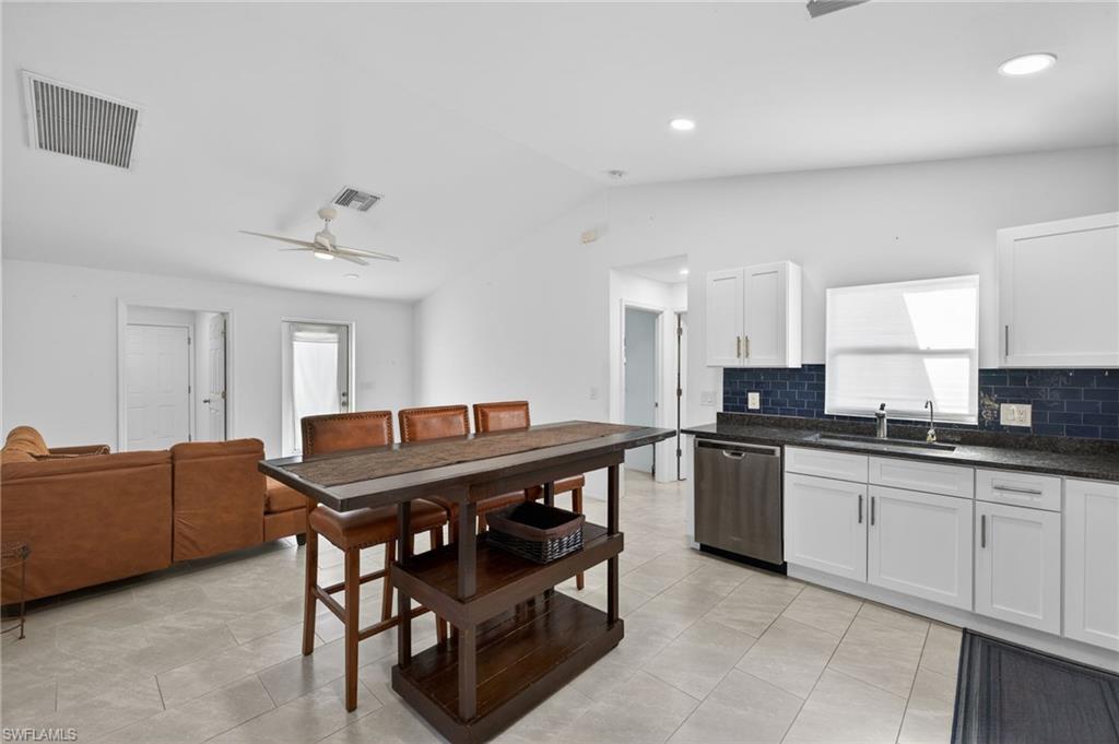 Kitchen featuring a ceiling fan, dishwasher, white cabinetry, tasteful backsplash, and dark stone counters