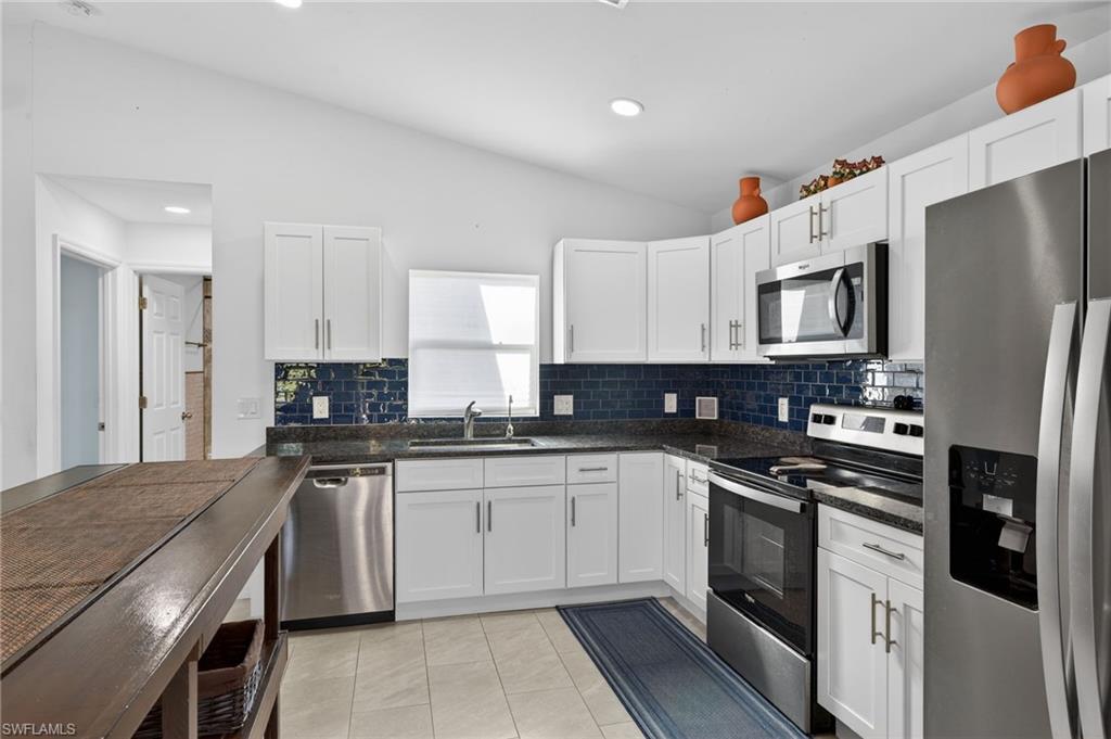 Kitchen featuring stainless steel appliances, white cabinets, lofted ceiling, dark stone countertops, and tasteful backsplash