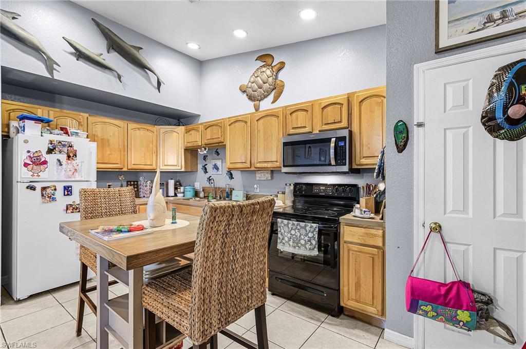 Kitchen featuring black electric range, freestanding refrigerator, stainless steel microwave, light tile patterned floors, and light countertops