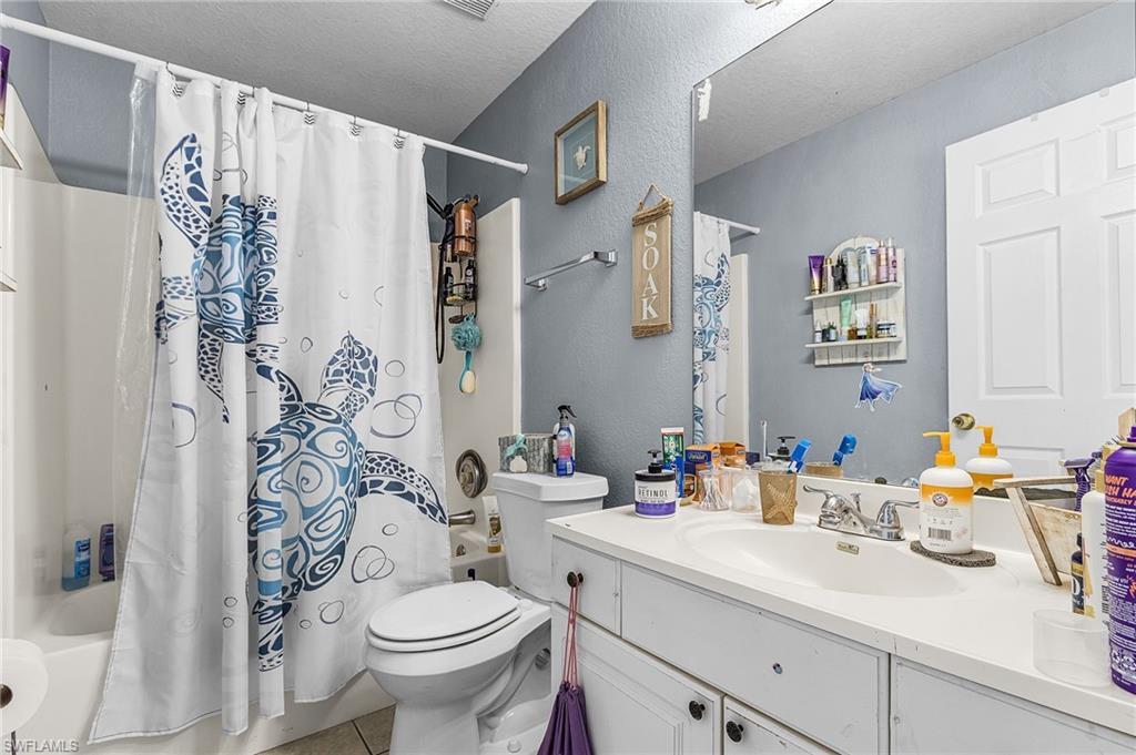 Bathroom featuring shower / tub combo with curtain, a textured wall, vanity, a textured ceiling, and light tile patterned flooring