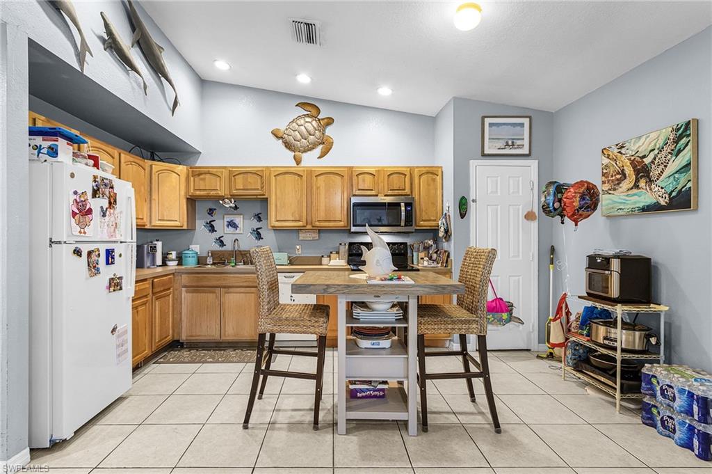 Kitchen with freestanding refrigerator, light countertops, vaulted ceiling, stainless steel microwave, and light tile patterned flooring