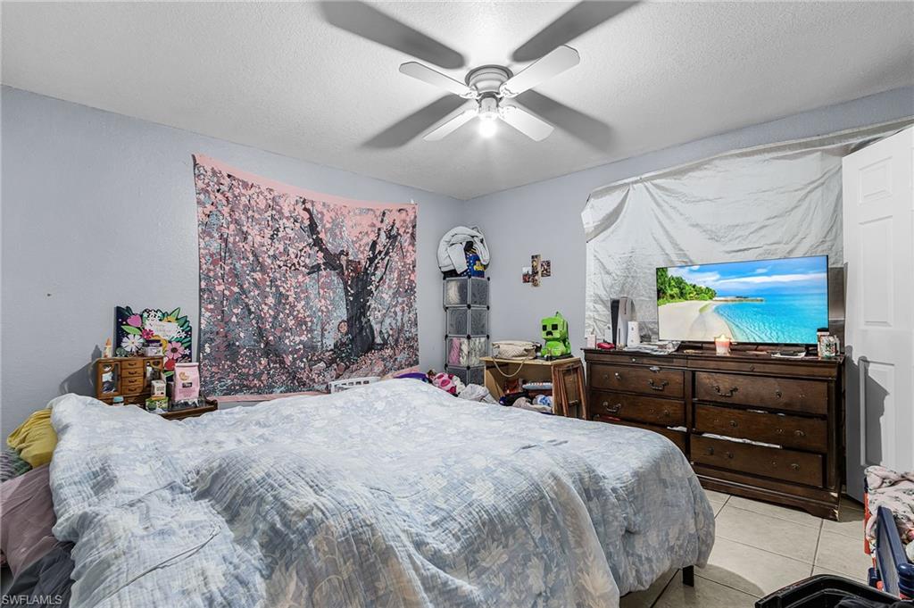 Bedroom with a ceiling fan, light tile patterned floors, and a textured ceiling