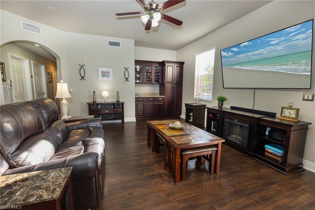 Living area with dark wood-type flooring, ceiling fan, and arched walkways