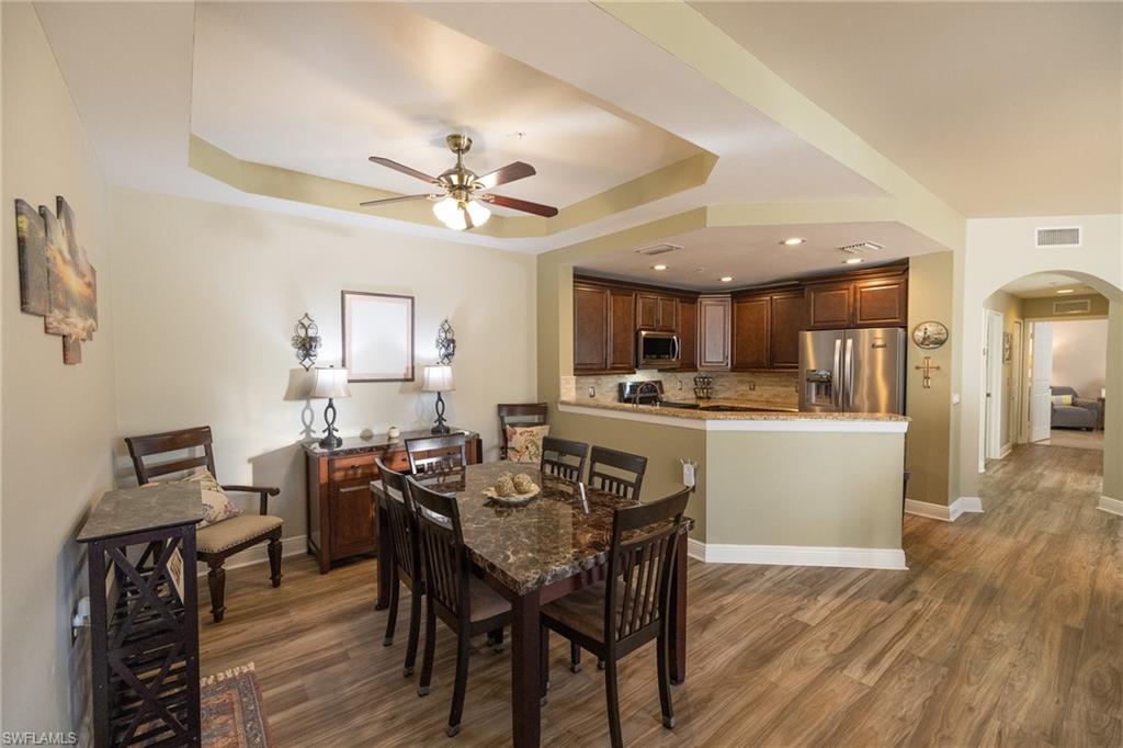 Dining room featuring arched walkways, dark wood finished floors, a ceiling fan, a tray ceiling, and recessed lighting