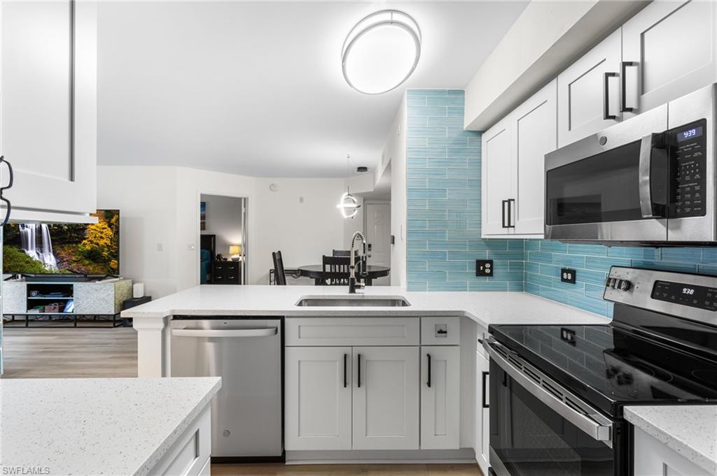 Kitchen with stainless steel appliances, a peninsula, white cabinetry, light stone counters, and open floor plan